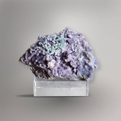 Front view of 335g Grape Agate cluster with dense lavender spheres and a pale blue-green center displayed on a clear block