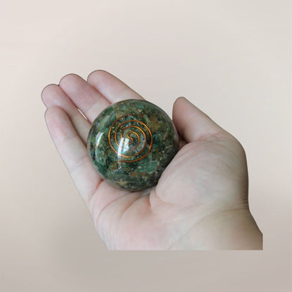 Two inch Green Aventurine orgonite sphere with copper spiral resting in a hand to show size and scale