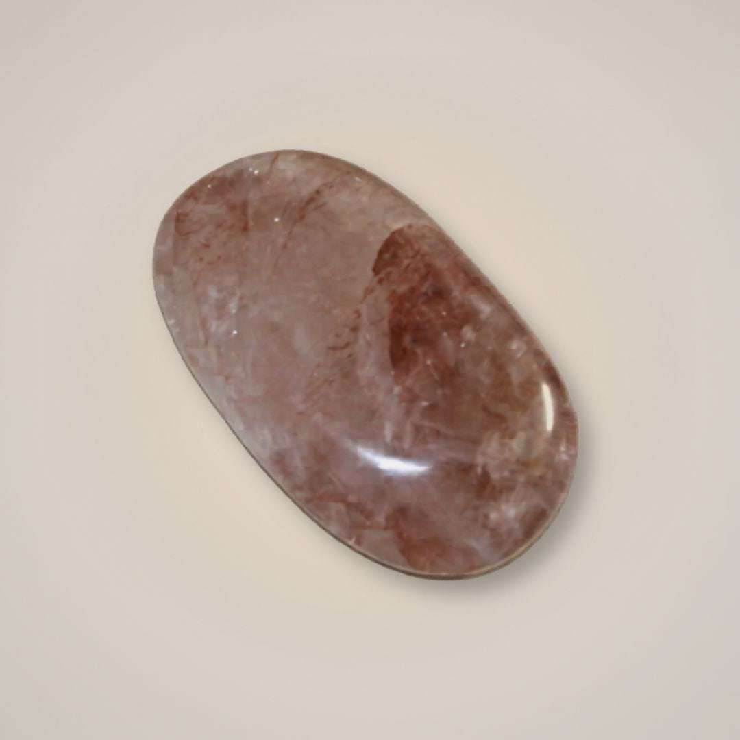 Polished hematoid quartz palm stone from Brazil with rose, rust-red, and smoky mineral inclusions on a neutral background.