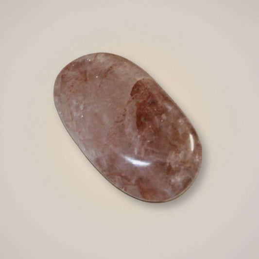 Polished hematoid quartz palm stone from Brazil with rose, rust-red, and smoky mineral inclusions on a neutral background.