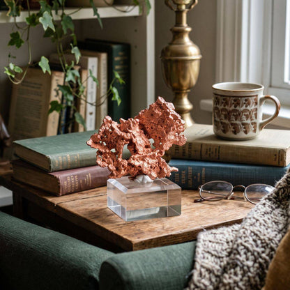 Sculptural native copper specimen from China displayed on a clear acrylic base in a reading nook with vintage books, greenery, and a ceramic mug.