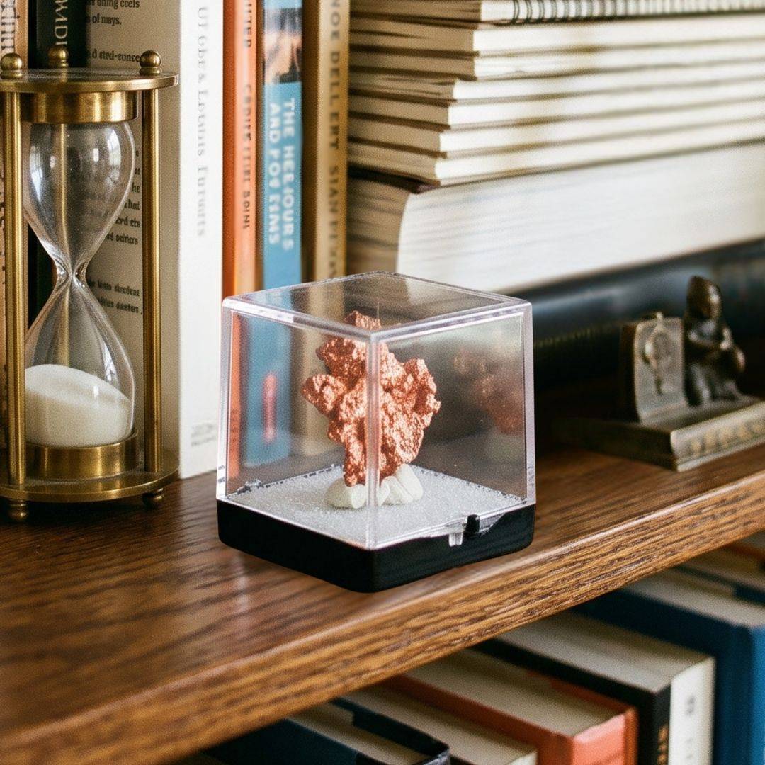 Native copper miniature specimen from China displayed inside a clear protective perky box on a wooden bookshelf beside books and a brass hourglass.