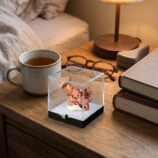 Native copper specimen from China displayed in a clear protective perky box on a wooden bedside table beside books, reading glasses, and a ceramic mug.