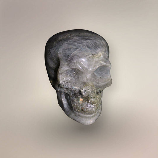 Hand-carved Labradorite skull from Madagascar with smoky gray coloring, internal veining, polished surface, and subtle golden flash.