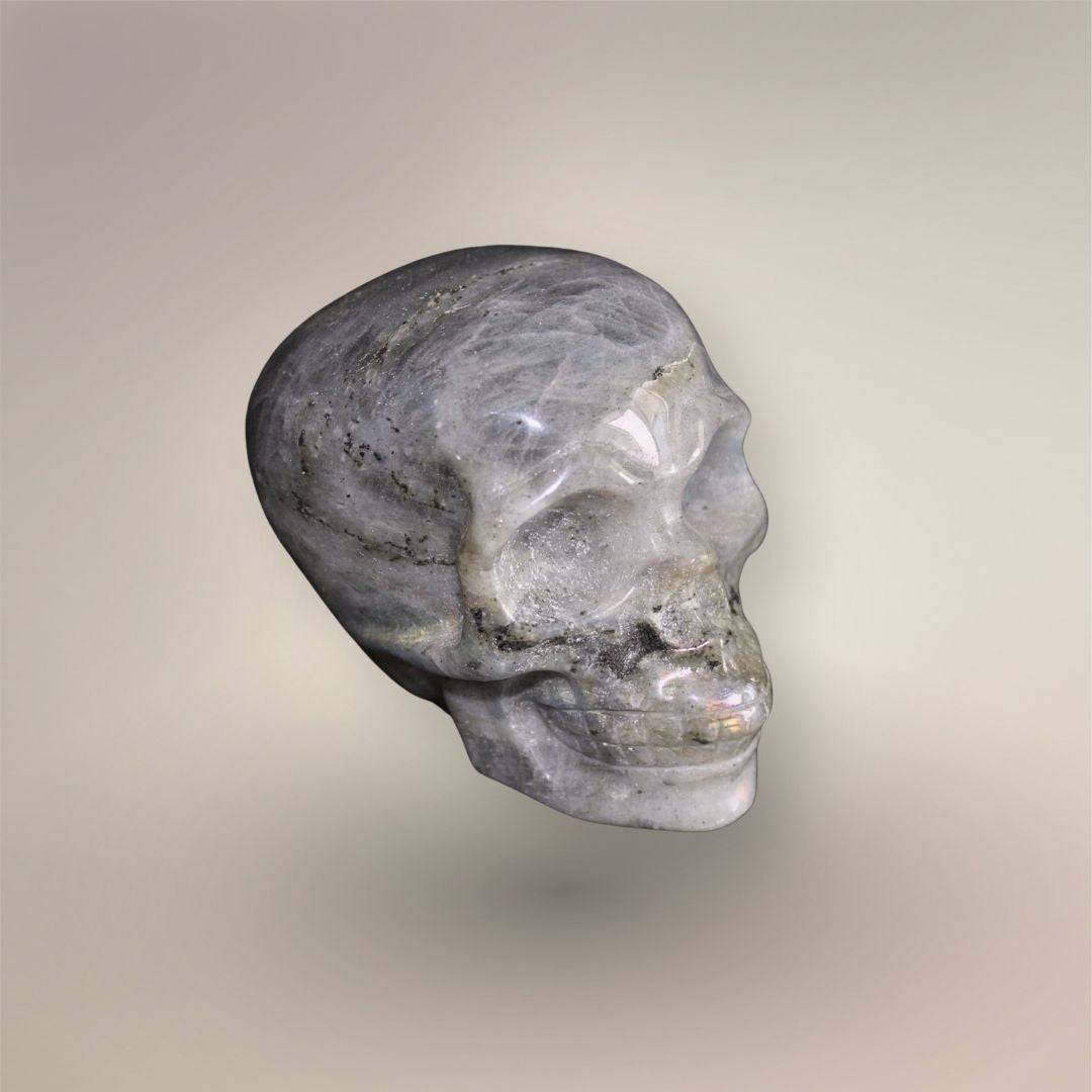 Side view of polished hand-carved Labradorite skull showing layered gray structure, inclusions, and subtle labradorescence.