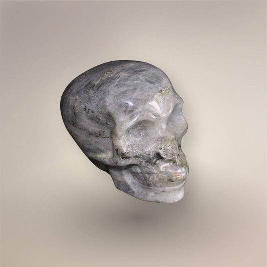 Side view of polished hand-carved Labradorite skull showing layered gray structure, inclusions, and subtle labradorescence.