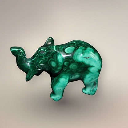 Side view of a polished Malachite elephant carving with a raised trunk, carved ear, rounded body, and circular green patterning.