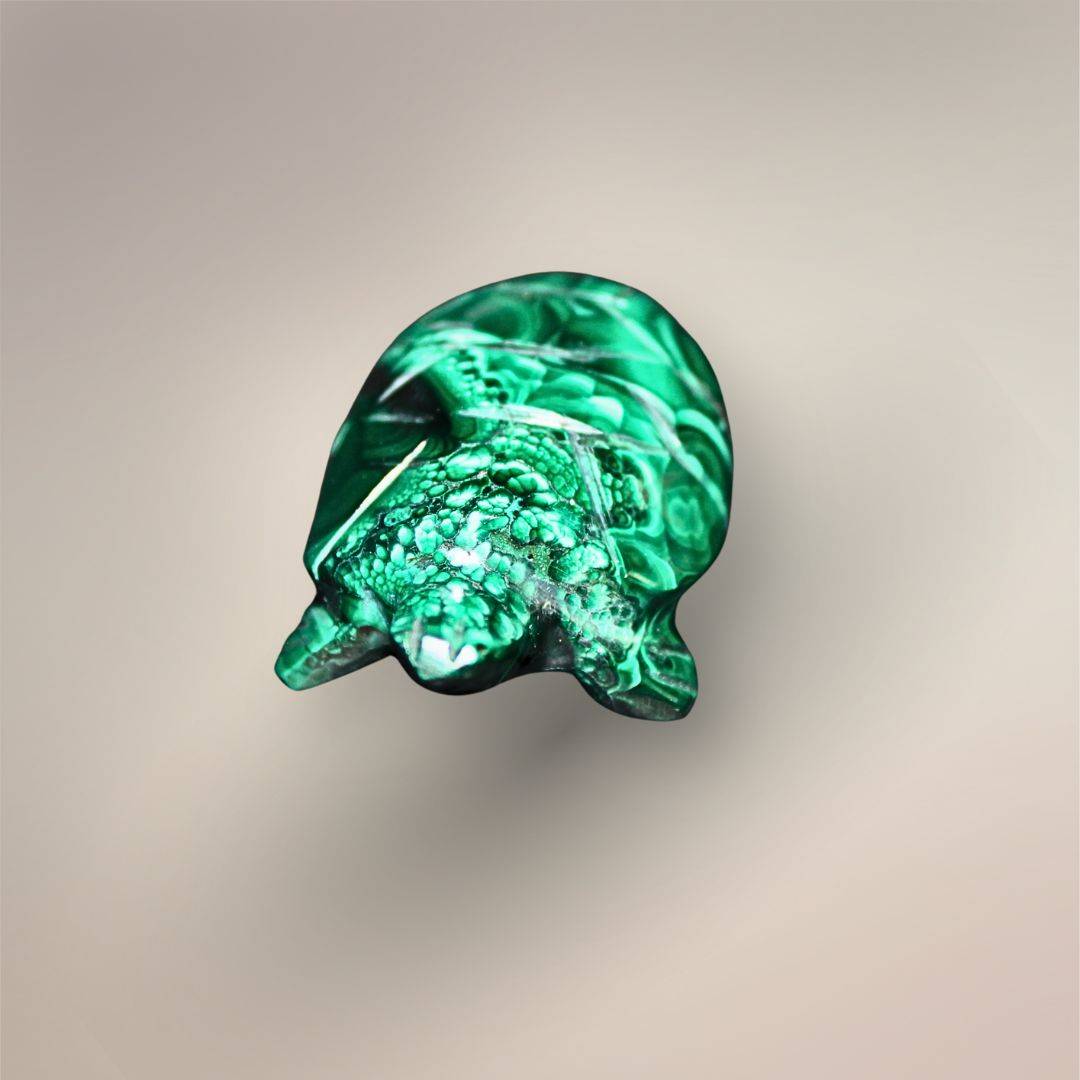 Front view of a polished Malachite turtle carving with a rounded head, extended flippers, carved shell details, and mixed banded and botryoidal-style patterns.