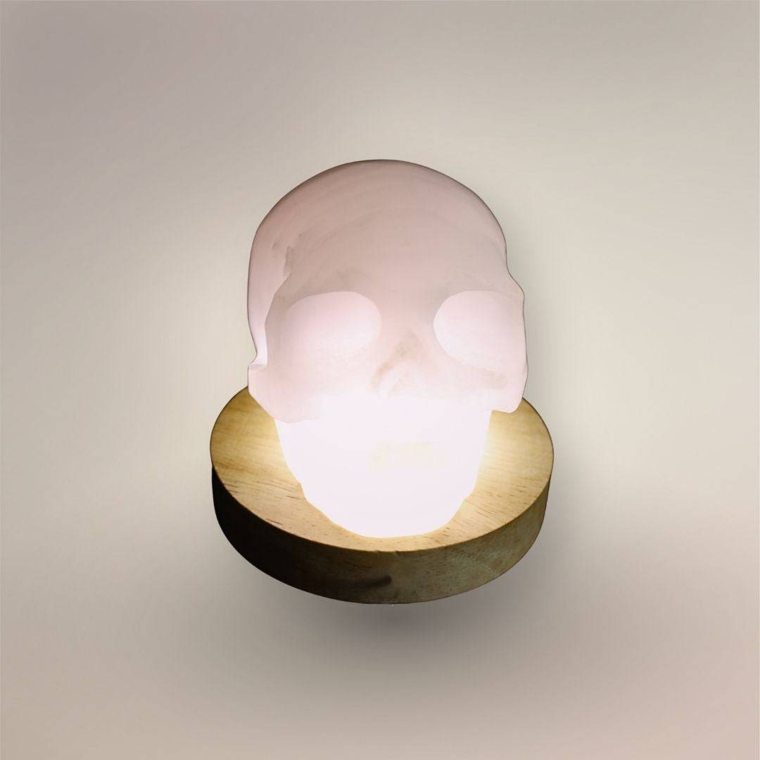 Pale pink mangano calcite skull from Mexico with polished carved facial details, on light stand