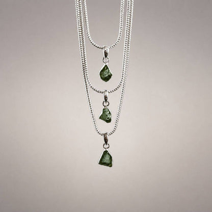 Three natural Moldavite pendants in varied irregular shapes and green tones, displayed on silver chains to show individual variation.