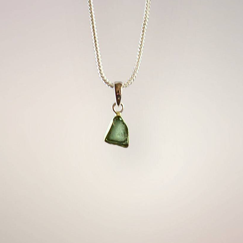 Front view of a translucent green Moldavite freeform pendant with natural surface texture and a polished sterling silver bail.