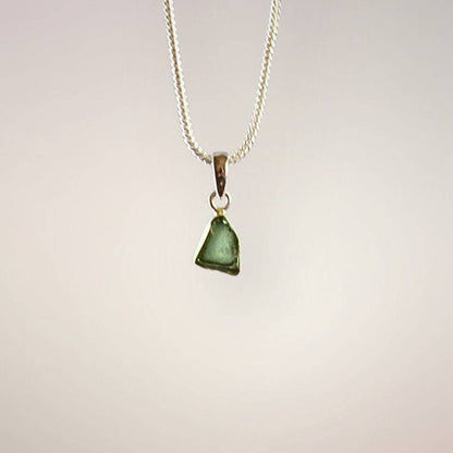 Front view of a translucent green Moldavite freeform pendant with natural surface texture and a polished sterling silver bail.