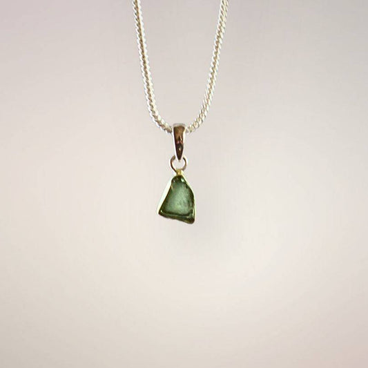 Front view of a translucent green Moldavite freeform pendant with natural surface texture and a polished sterling silver bail.