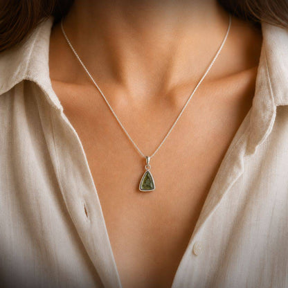 Small green Moldavite pendant worn at the collarbone on a fine silver chain with an open white linen shirt.