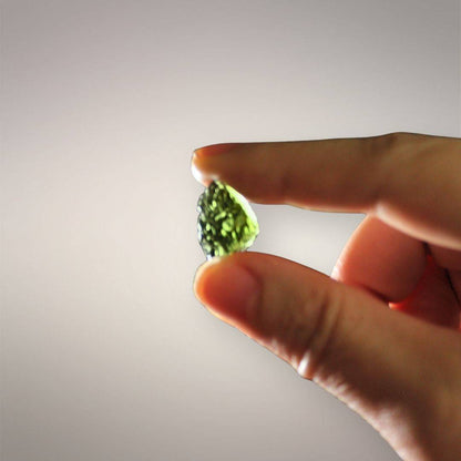 Backlit in-hand scale view of Czech Republic Moldavite showing its thumbnail size, tapered outline, and bright yellow-green transmitted color.