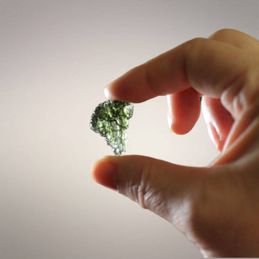 In-hand scale view of Czech Republic Moldavite held against light, showing its thin profile, tear-shaped outline, and translucent green body.