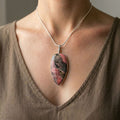 Necklace with a rhodonite pendant worn by a person in a brown top.