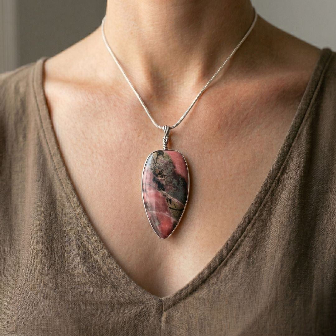 Necklace with a rhodonite pendant worn by a person in a brown top.