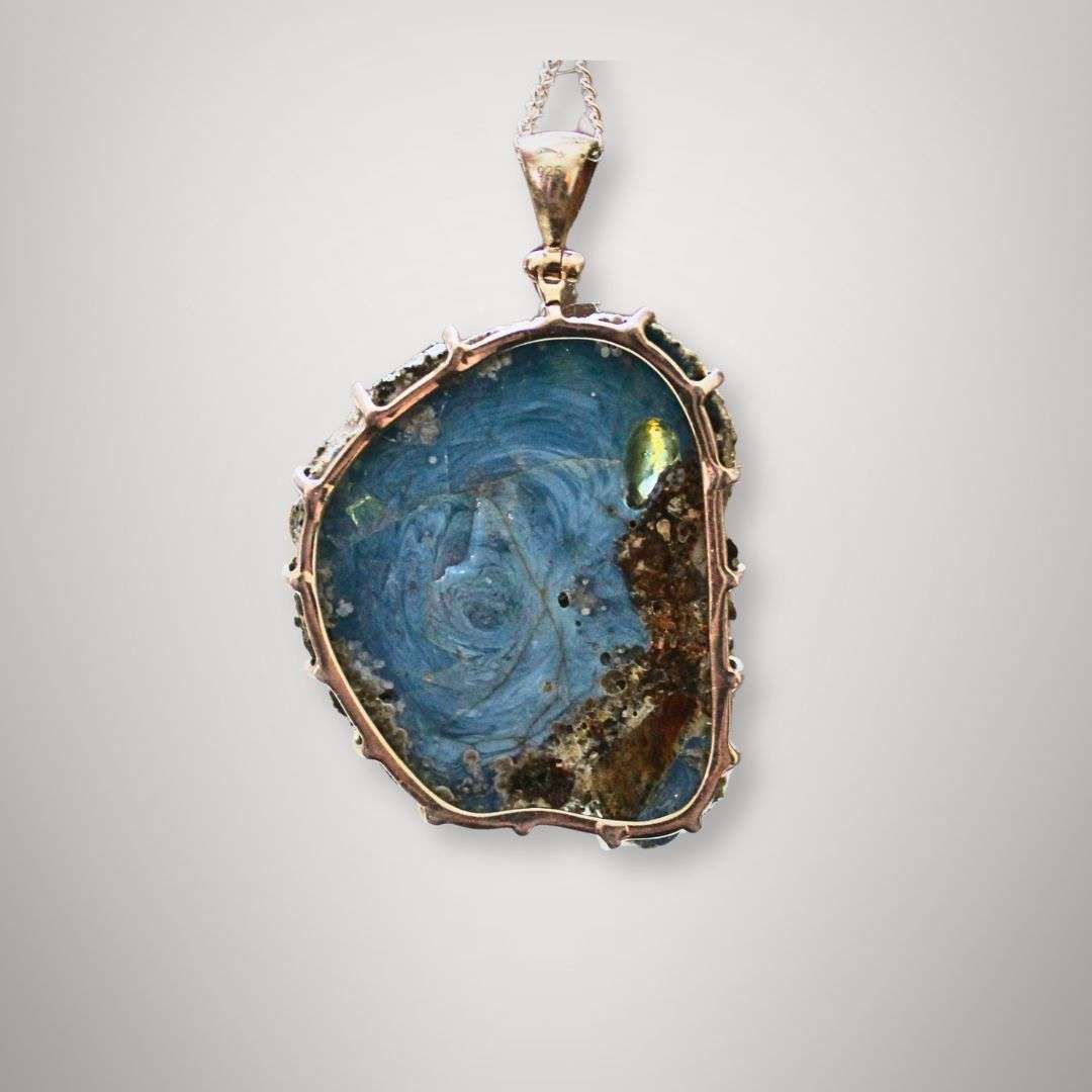 Hand holding Swedish slag glass pendant with vortex pattern in sterling silver