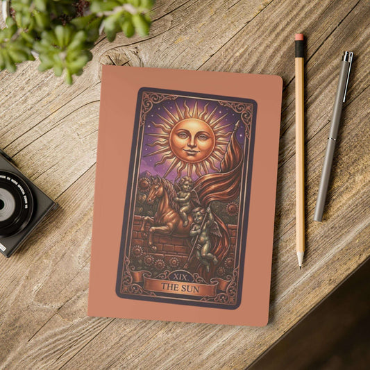 Notebook with 'The Sun' tarot card design on a wooden surface with a pen and pencil.