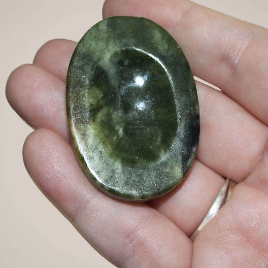 Small nephrite palm stone from Pakistan held in hand, showing smooth polish, oval shape, and carved thumb groove.