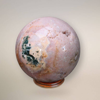 Pink amethyst sphere showing pale pink coloration, an exposed crystalline geode cavity, and dark green inclusions on a wood display base.