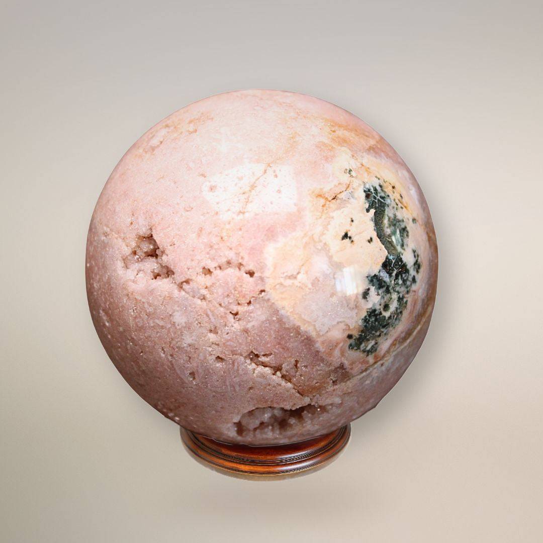 Reverse view of the pink amethyst sphere displaying textural variations, a small druzy pocket, and deep green surface patterning.