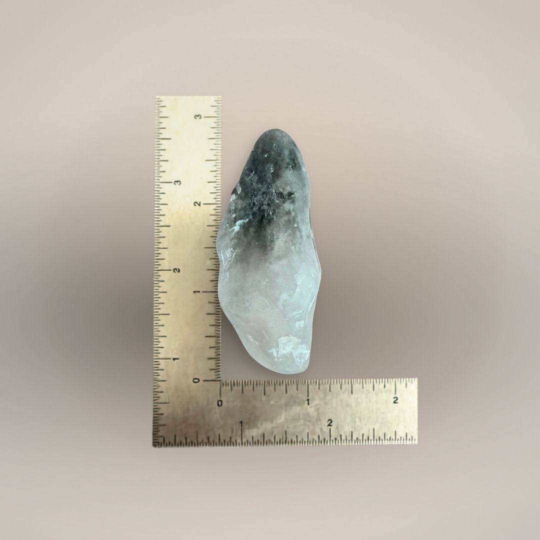 Prasiolite freeform palm stone beside an inch ruler, showing an irregular elongated shape measuring approximately 2.5 to 3 inches.
