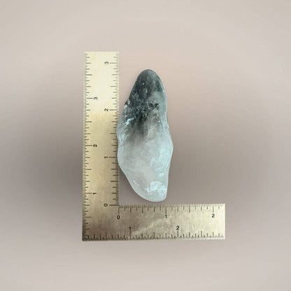 Prasiolite freeform palm stone beside an inch ruler, showing an irregular elongated shape measuring approximately 2.5 to 3 inches.