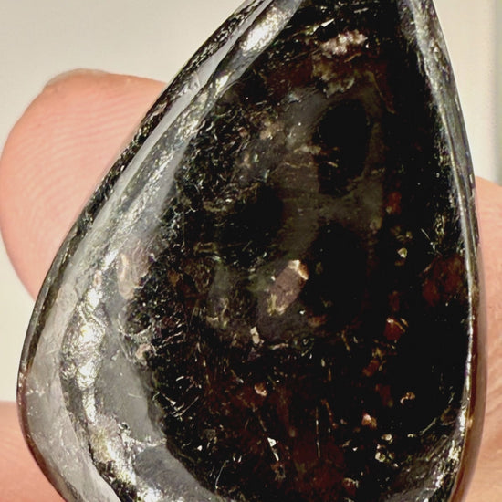 Close up view of 25ct Nuummite tear drop cabochon with golden flashes