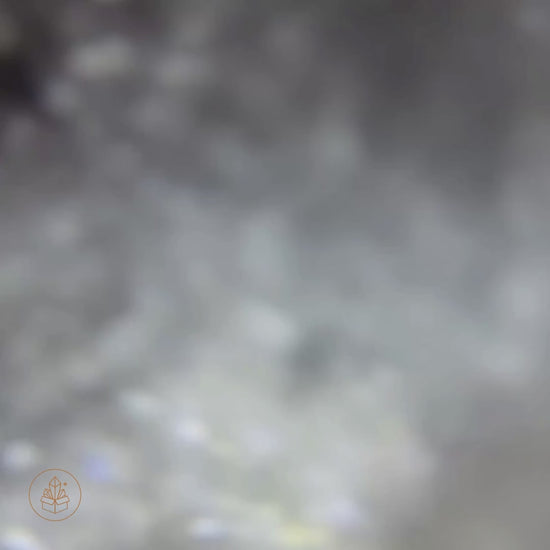 Close-up video of an 80 mm Clear Quartz sphere from Madagascar on a wooden display base, revealing natural internal veils, featherlike fractures, and subtle rainbow light refractions as the camera moves closer.