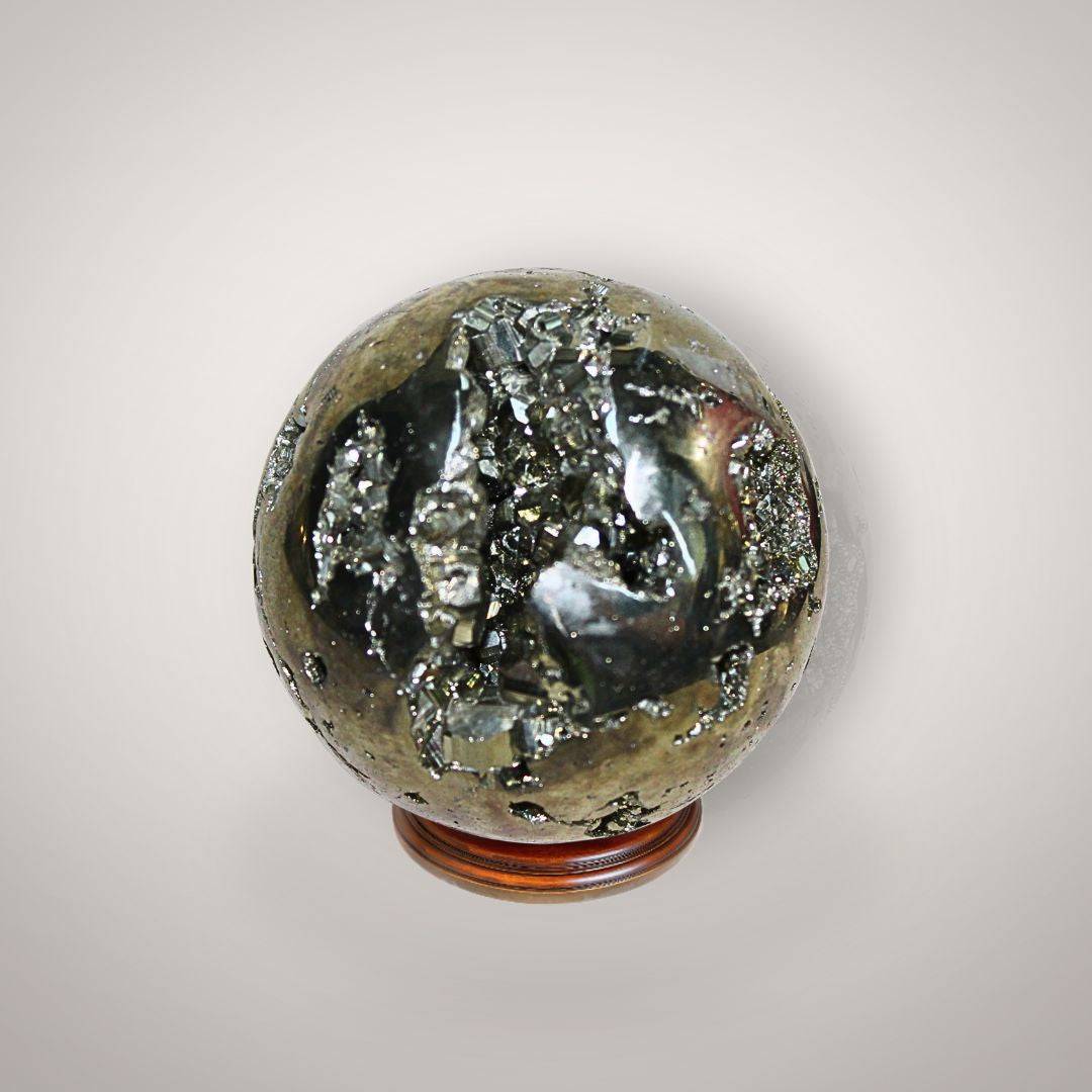 Pyrite geode sphere from Peru held in hand, showing metallic golden crystal pockets, natural matrix, and approximate palm-size scale.