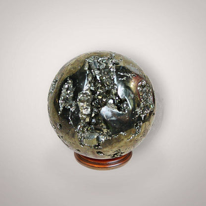 Pyrite geode sphere from Peru held in hand, showing metallic golden crystal pockets, natural matrix, and approximate palm-size scale.