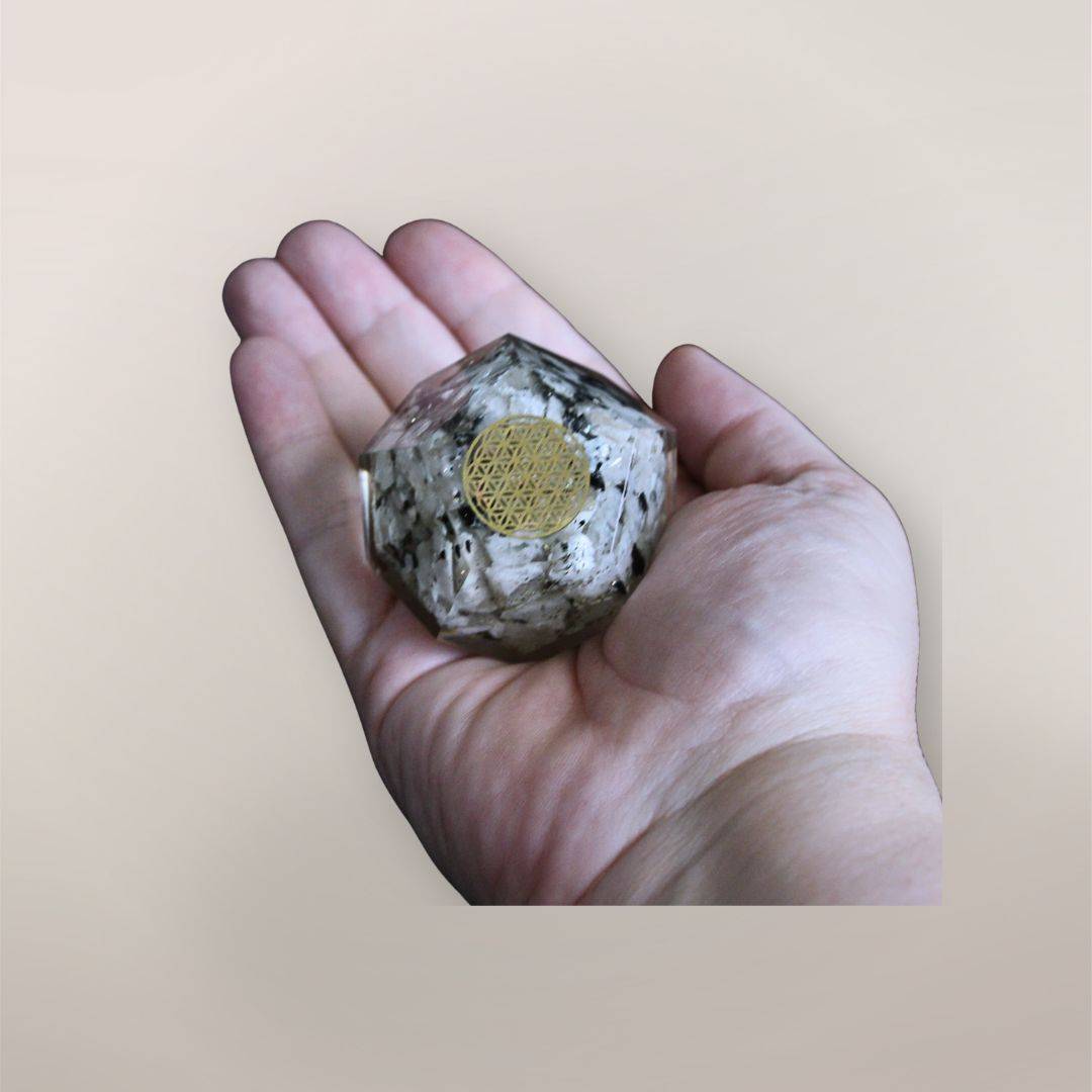 Two inch Rainbow Moonstone orgonite dodecahedron with golden Flower of Life symbol resting in a hand to show size and scale