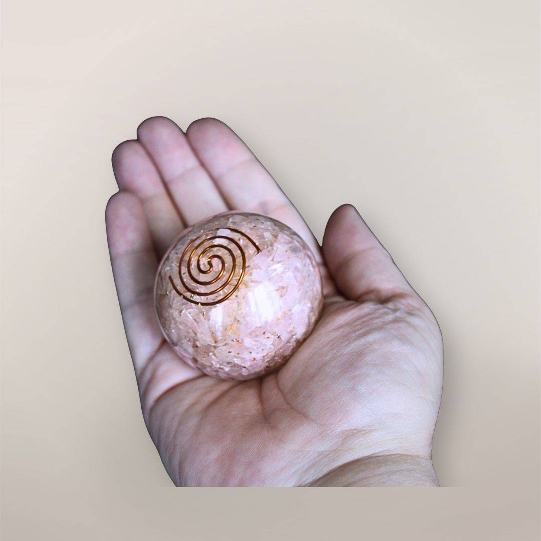 Two inch Rose Quartz orgonite sphere with copper spiral resting in a hand to show size and scale