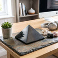 Large polished Shungite pyramid styled on a stone mat with crystals on a desk