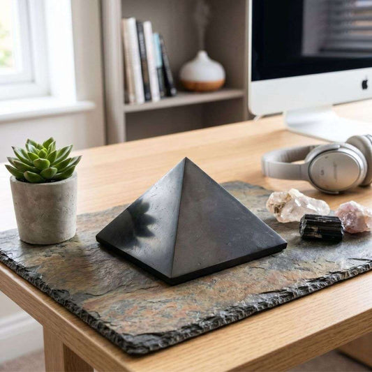 Large polished Shungite pyramid styled on a stone mat with crystals on a desk