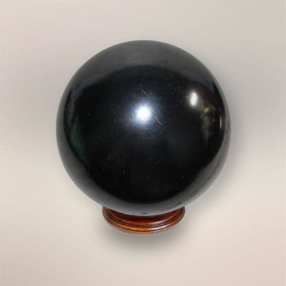 Polished black Shungite sphere 75mm from Russia on wooden display stand, shown against a neutral background