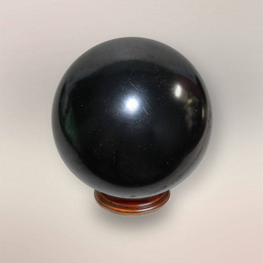 Polished black Shungite sphere 75mm from Russia on wooden display stand, shown against a neutral background