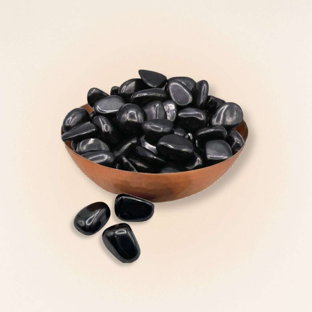 Bowl filled with polished black Shungite tumbled stones from Russia on a cream background.