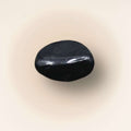 Single polished black Shungite tumbled stone from Russia shown on a soft cream background.