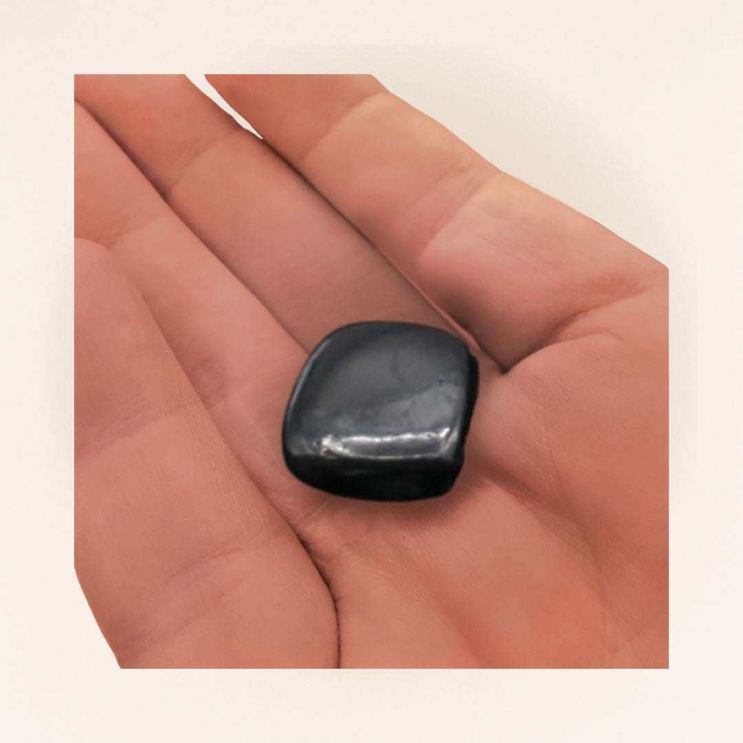 Polished Shungite tumbled stone resting in a hand to show approximate .5 to 1 inch size.