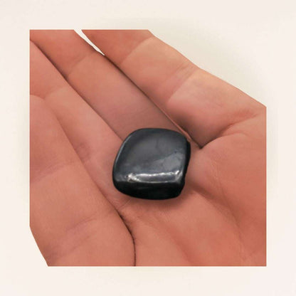 Polished Shungite tumbled stone resting in a hand to show approximate .5 to 1 inch size.