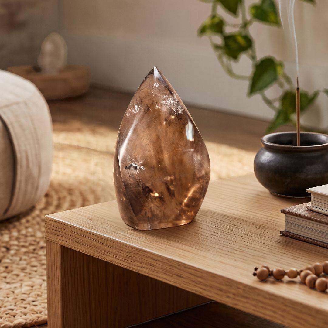 Brazilian Smoky Quartz Flame displayed on a wooden table beside incense and decorative books in a warm, neutral interior.