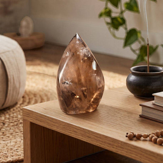 Brazilian Smoky Quartz Flame displayed on a wooden table beside incense and decorative books in a warm, neutral interior.
