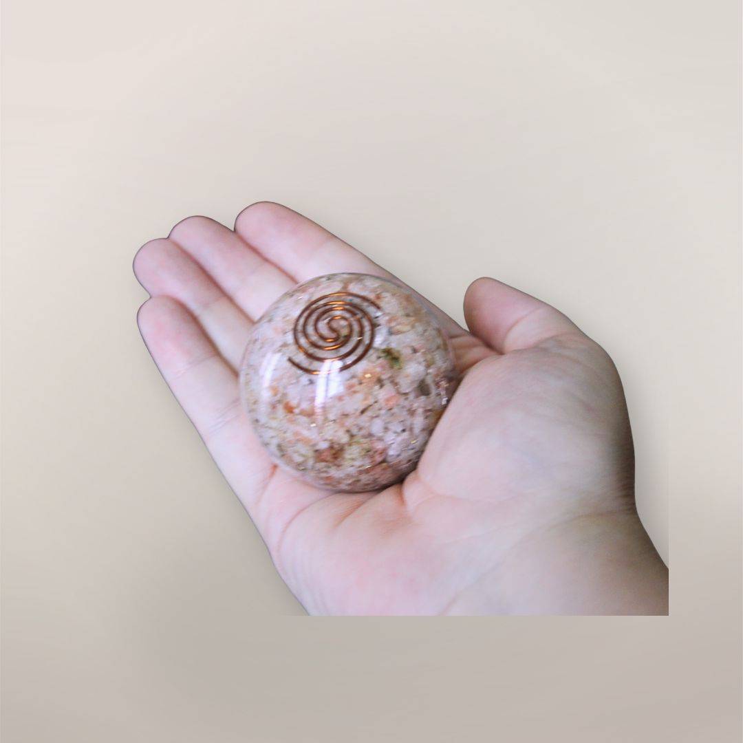 Two inch Sunstone orgonite sphere with copper spiral resting in a hand to show size and scale