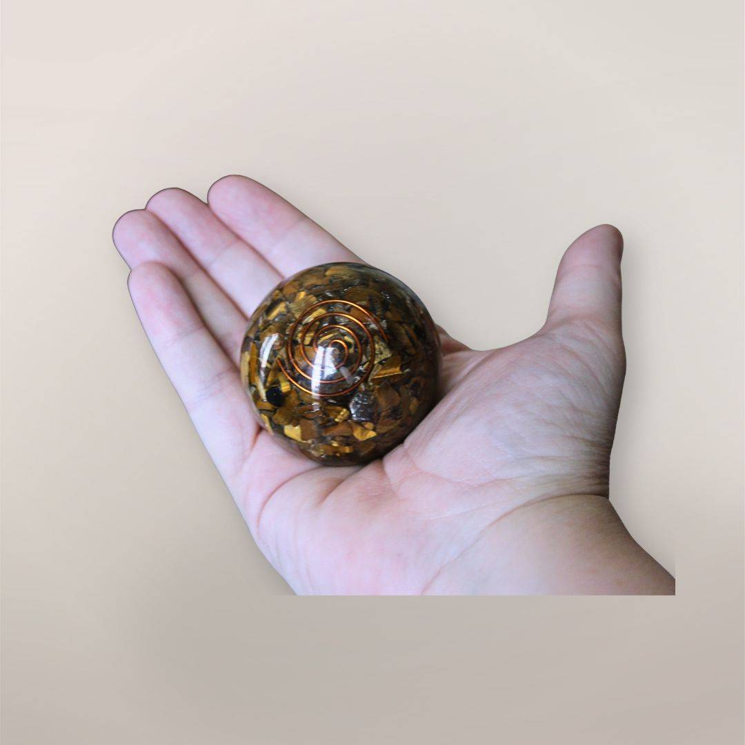 Two inch Tiger’s Eye orgonite sphere with copper spiral resting in a hand to show size and scale