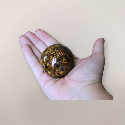 Two inch Tiger’s Eye orgonite sphere with copper spiral resting in a hand to show size and scale