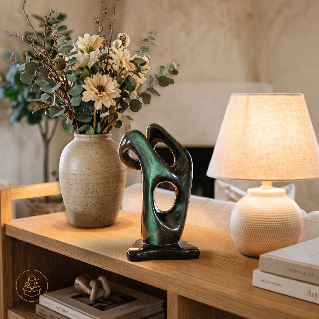 Green Flash Velvet Rainbow Obsidian sculpture displayed on a wooden console beside a ceramic vase, flowers, and illuminated lamp.