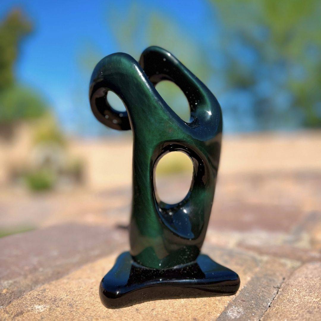 Outdoor view of Mexican Velvet Rainbow Obsidian sculpture showing green optical sheen in natural sunlight.